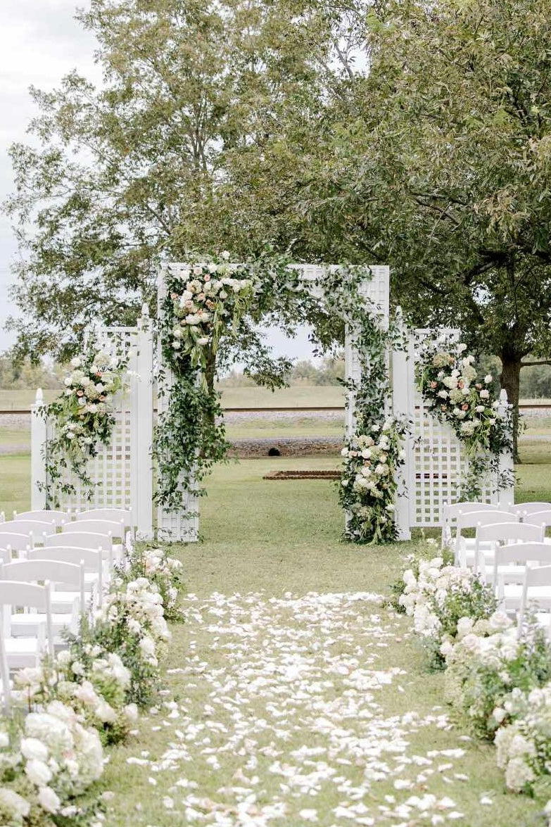 Decorative wedding arch with floral arrangements on a grassy field.